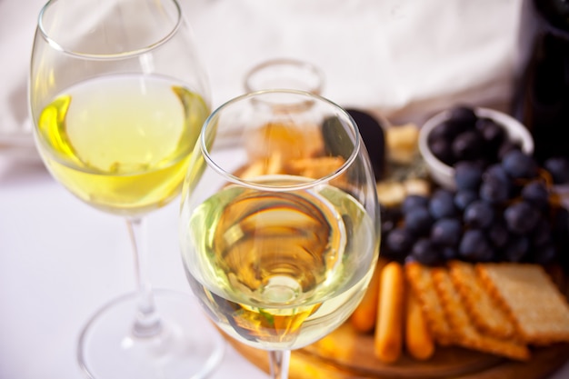 Dos copas de vino blanco y plato con variedad de quesos y frutas