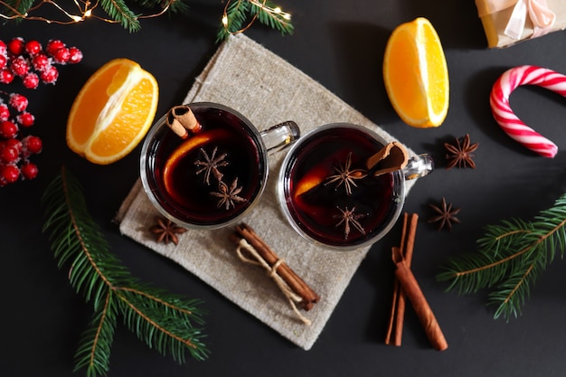 Dos copas de vino caliente con canela y naranjas sobre un fondo festivo de Navidad