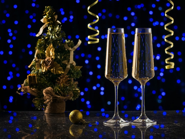 Dos copas de vino espumoso y un árbol de Navidad con luces bokeh azules. Vispera de Año Nuevo