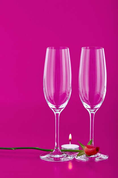 Foto dos copas de vino con una flor de rosa y una vela romántica