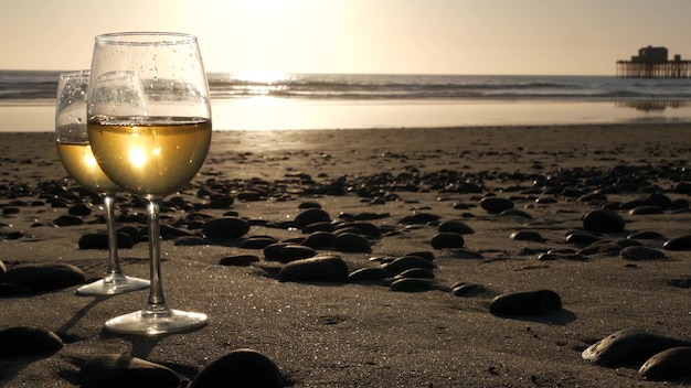 Dos copas de vino en la playa del océano. Copas con vino blanco para cita romántica, agua de mar. Olas al atardecer.