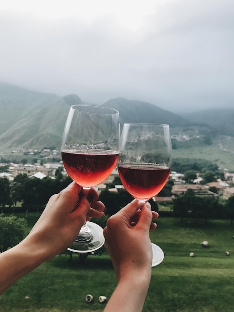 Dos copas de vino de rosas en dos manos en frente de las montañas