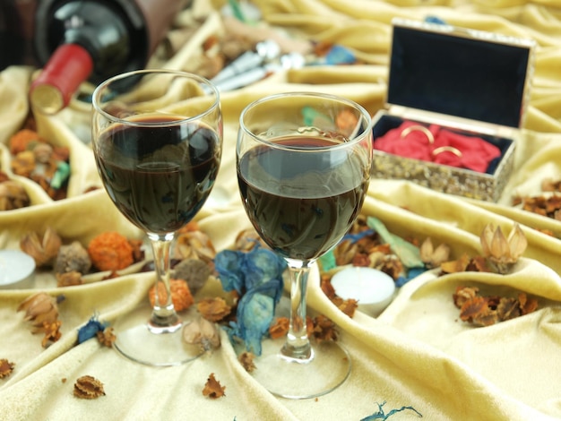 Dos copas de vino se sientan en una mesa con una caja de dulces rojos al fondo.