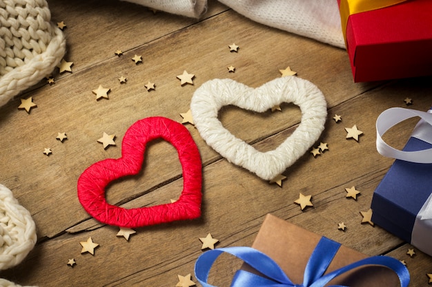 Dos corazones, bufanda tejida, cajas de regalo, guirnalda luminosa sobre un fondo de madera.