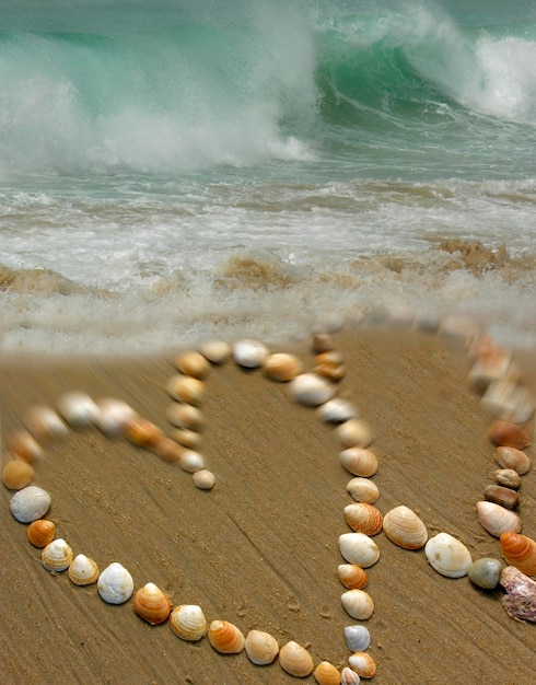 Dos corazones hechos de conchas en una playa con fuertes olas en el fondo