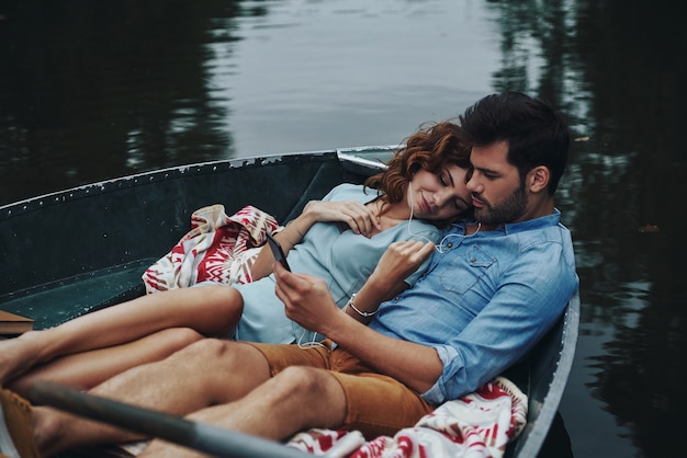 Dos corazones llenos de amor. Hermosa joven pareja escuchando música mientras está sentado en el barco al aire libre