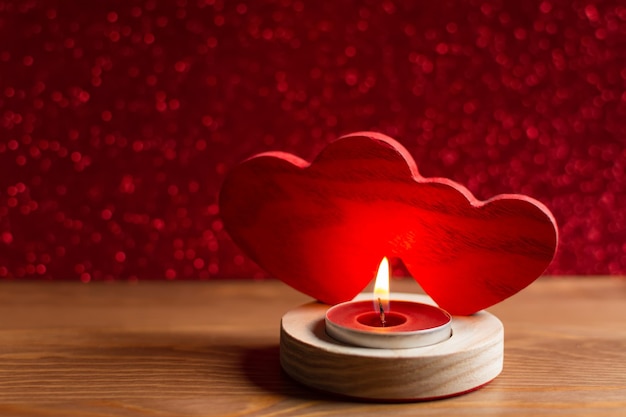 Dos corazones de madera y una vela encendida sobre la mesa. Fondo rojo borroso con pequeño bokeh