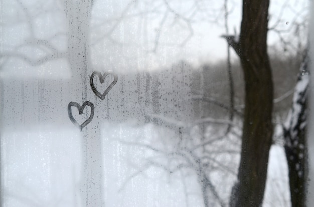 Dos corazones pintados en un vidrio empañado en invierno