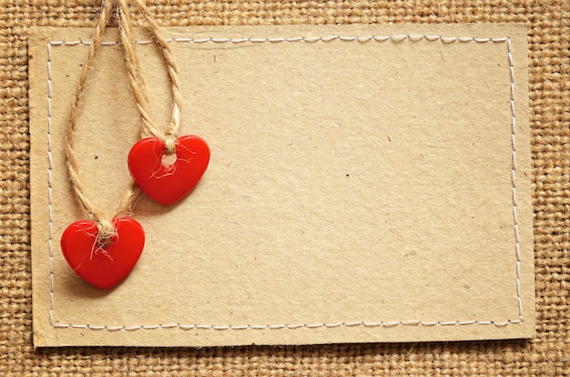 Dos corazones de plástico rojo y tarjeta de cartón sobre un fondo de lienzo
