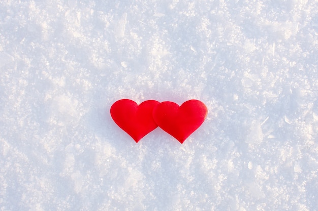 Dos corazones rojos sobre la nieve blanca limpia en un día soleado de invierno.