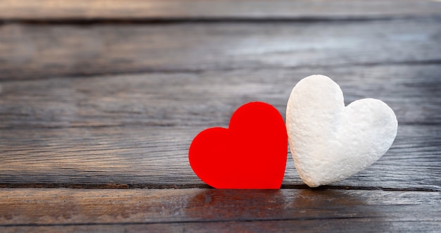 Foto dos corazones sobre un fondo oscuro. un par de corazones diferentes rojo y blanco sobre una superficie de madera