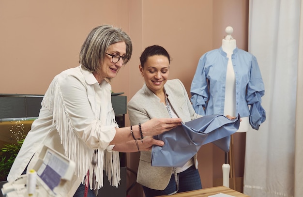 Dos costureras en el trabajo Costureras calificadas mirando telas discutiendo la calidad de los textiles Colegas en el taller de costura moderno mejorando el proceso de producción juntos