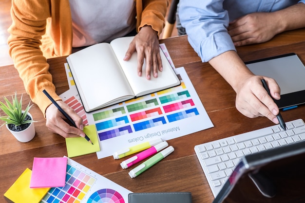 Dos creativos diseñadores gráficos que trabajan en la selección de colores y muestras de colores, dibujando en una tableta gráfica.