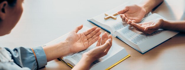 Foto dos creyentes rezan juntos en la santa biblia con una cruz de madera colocada burgeoning