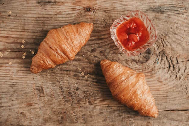 Dos croissant con mermelada de fresa sobre un fondo de madera vista superior Desayuno dulce y abundante con croissants