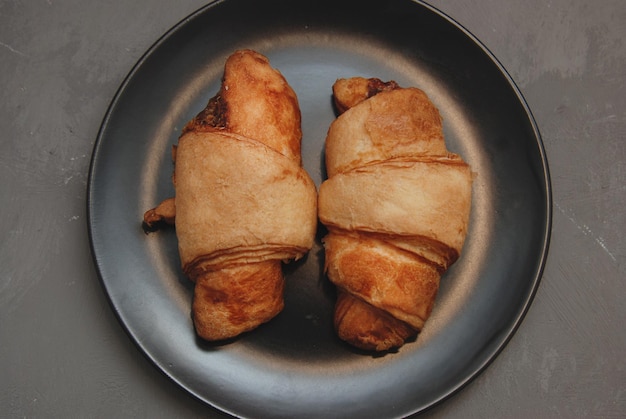 Dos croissants aislados en placa negra sobre fondo gris oscuro. vista superior. Desayuno.