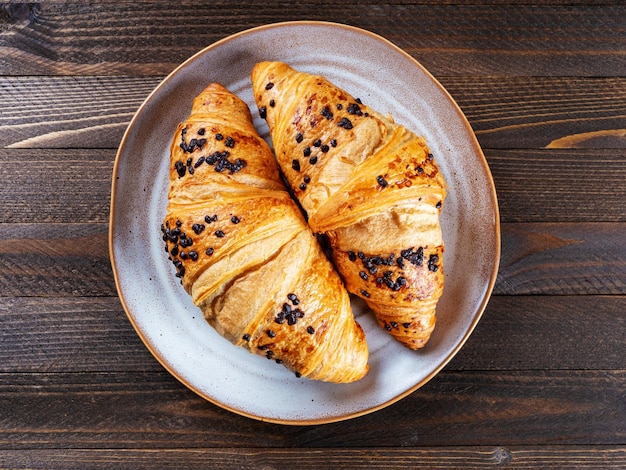 Dos croissants de chocolate en un plato marrón sobre un fondo de madera