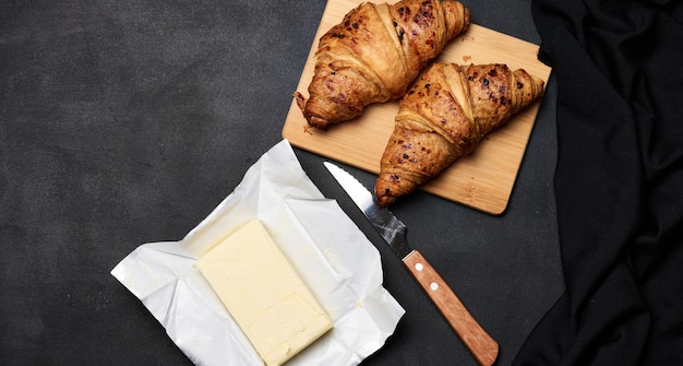 Dos croissants horneados, un paquete de mantequilla y un cuchillo en una vista superior de fondo negro