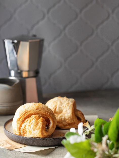 Dos croissants en plato de cerámica con cafetera y flores florecientes Acogedor concepto de desayuno de buenos días