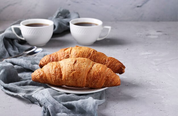 Foto dos croissants recién hechos y dos tazas de café sobre un fondo de hormigón gris claro. concepto de desayuno o almuerzo.