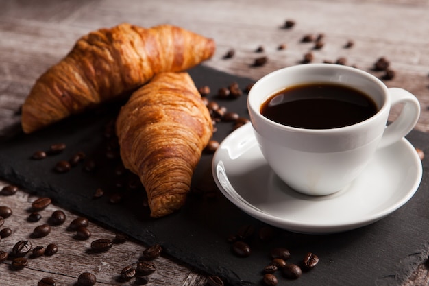 Dos croissants recién hechos y una taza de café en la mesa de piedra oscura. Postre delicioso.