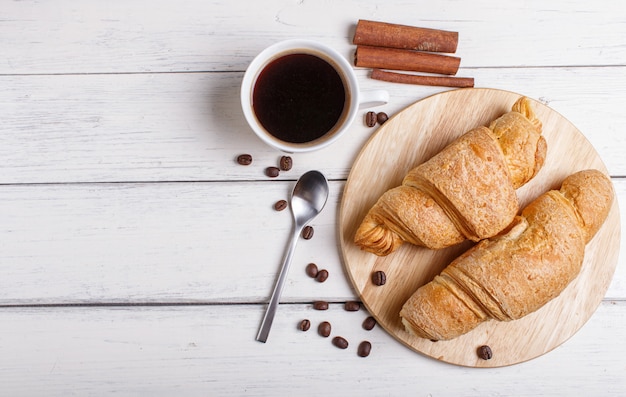 Dos croissants con la taza de café en tablero de madera de la cocina en el fondo de madera blanco