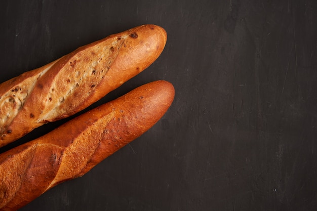 Dos crujientes baguettes francesas mienten el fondo negro oscuro de la tabla