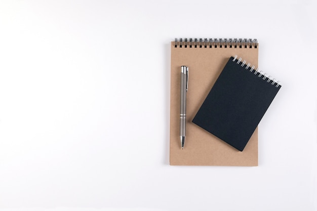 Dos cuadernos de espiral en blanco apilados sobre un fondo blanco junto a un bolígrafo automático. Bloc de notas con hojas negras y recicladas. Educación, oficina.