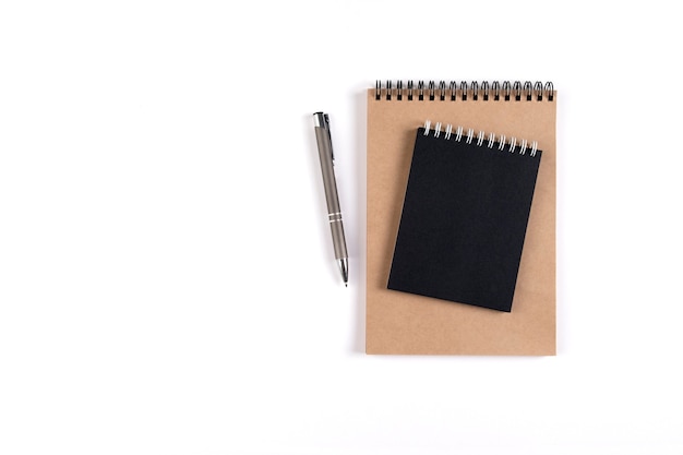 Dos cuadernos de espiral en blanco apilados sobre un fondo blanco junto a un bolígrafo automático. Bloc de notas con hojas negras y recicladas. Educación, oficina.