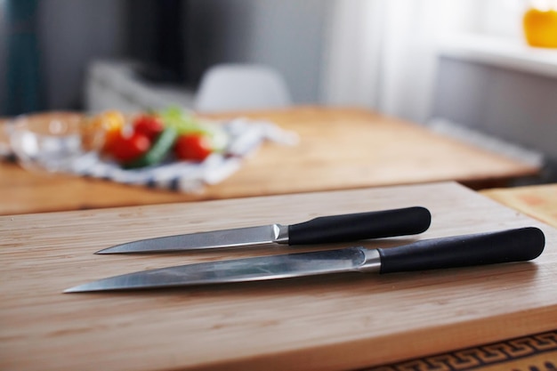 Dos cuchillos en primer plano para cocinar verduras se encuentran sobre una mesa de madera