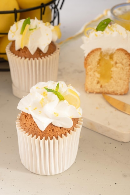 Foto dos cupcakes con crema de limón encima y un trozo de tarta de fondo.