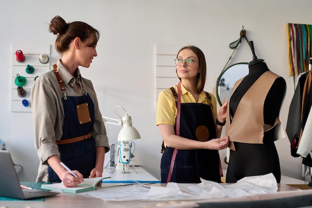 Foto dos curtidoras creativas en ropa de trabajo que consultan sobre un nuevo modelo de ropa