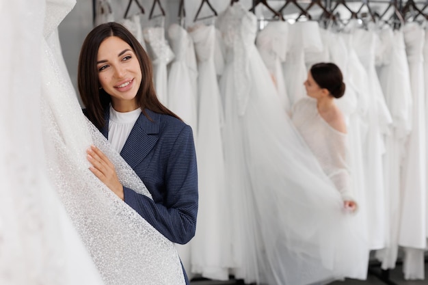 Foto dos damas de honor de una amiga eligen un vestido de novia en el salón.