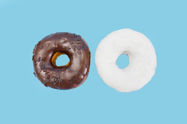 Dos deliciosas donas con glaseado de chocolate blanco y negro aislado sobre un fondo azul.