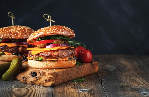 Dos deliciosas hamburguesas caseras de carne, queso y verduras en una vieja mesa de madera.