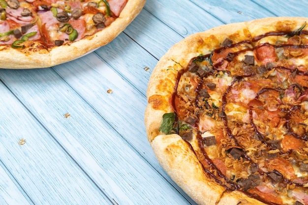 Dos deliciosas pizzas grandes diferentes sobre un fondo de madera azul.