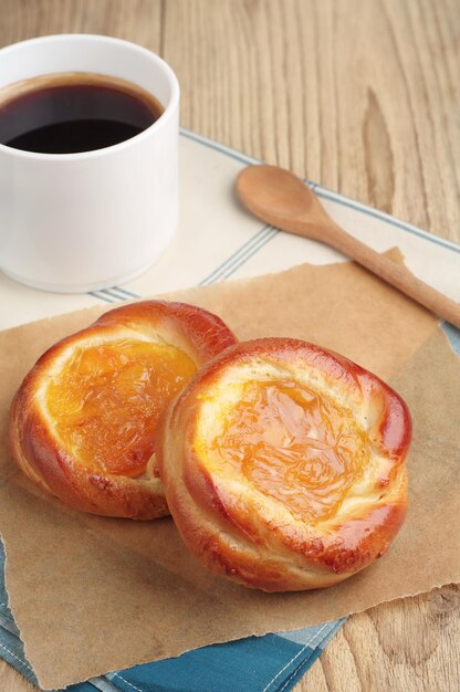 Dos deliciosos bollos con mermelada y una taza de café caliente en una mesa de madera rústica