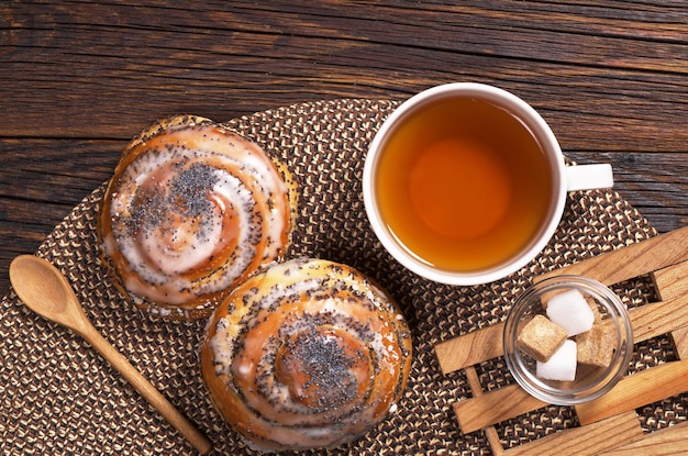 Dos deliciosos bollos con semillas de amapola y una taza de té en la vista superior de la mesa de madera rústica