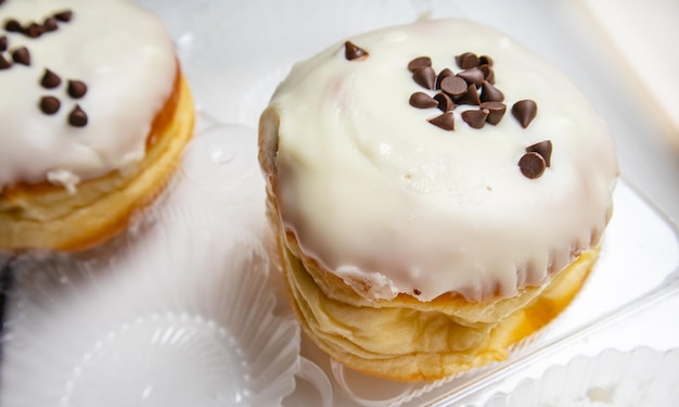 Dos deliciosos donuts con azúcar glaseado y chispas de chocolate sobre un fondo blanco en un recipiente de plástico transparente