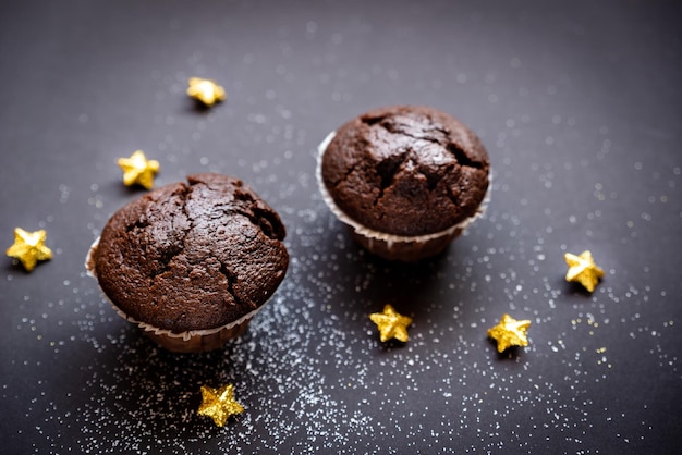 Dos deliciosos muffins de chocolate rodeados de estrellas doradas y polvo blanco sobre un fondo de papel negro