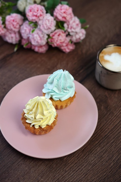 Dos deliciosos pasteles de crema dulce en un plato rosa con crema amarilla y azul se sientan en una mesa de madera.