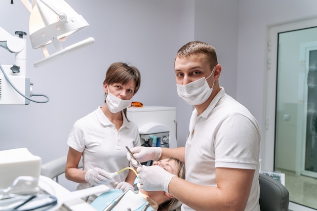 Dos dentistas examinan los dientes del paciente para el tratamiento posterior. Armario de estomatología moderno.