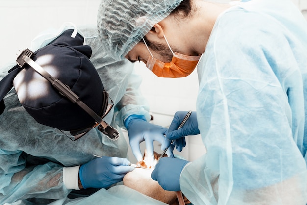 Dos dentistas masculinos realizan una operación en un paciente. Cirugía en odontología. Uniforme profesional y equipamiento de un dentista.