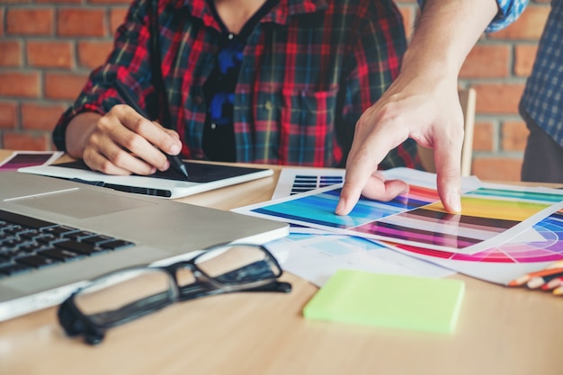 Dos diseñadores gráficos dibujan en una tableta gráfica y una guía de paleta de colores en el lugar de trabajo