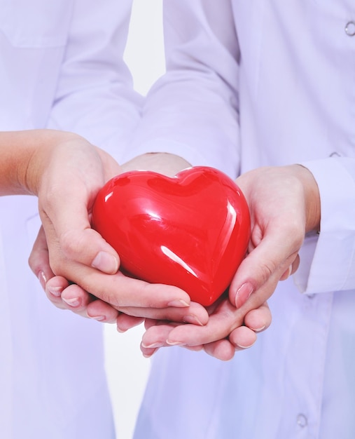 Dos doctora sosteniendo un corazón rojo aislado sobre fondo blanco.