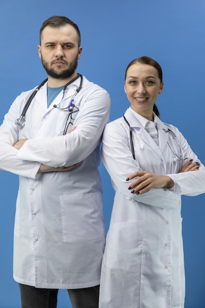 Foto dos doctores atractivos de pie mira a la cámara sobre fondo azul.