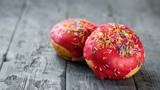 Dos donas de color rojo brillante sobre una mesa de madera negra