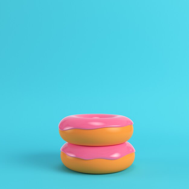 Dos donas con glaseado rosa sobre fondo azul brillante