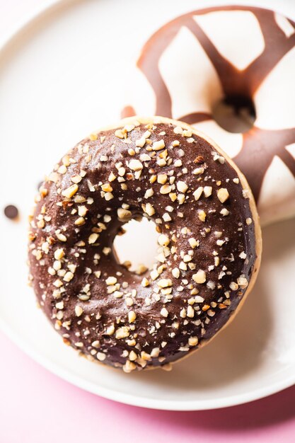 Dos donuts con glaseado de chocolate y cacahuetes sobre un fondo rosa Cerrar