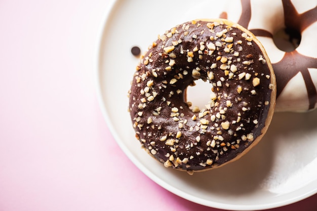 Dos donuts con glaseado de chocolate y maní sobre un fondo rosa Vista superior